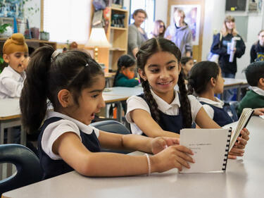 two female elementary students sitting at desk looking at books made for them