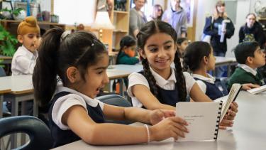 two female elementary students sitting at desk looking at books made for them