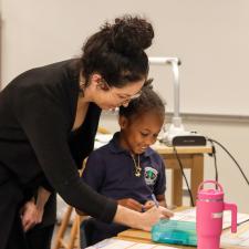 Teacher supporting student at their desk with class assignment. Student has a smile on her face.